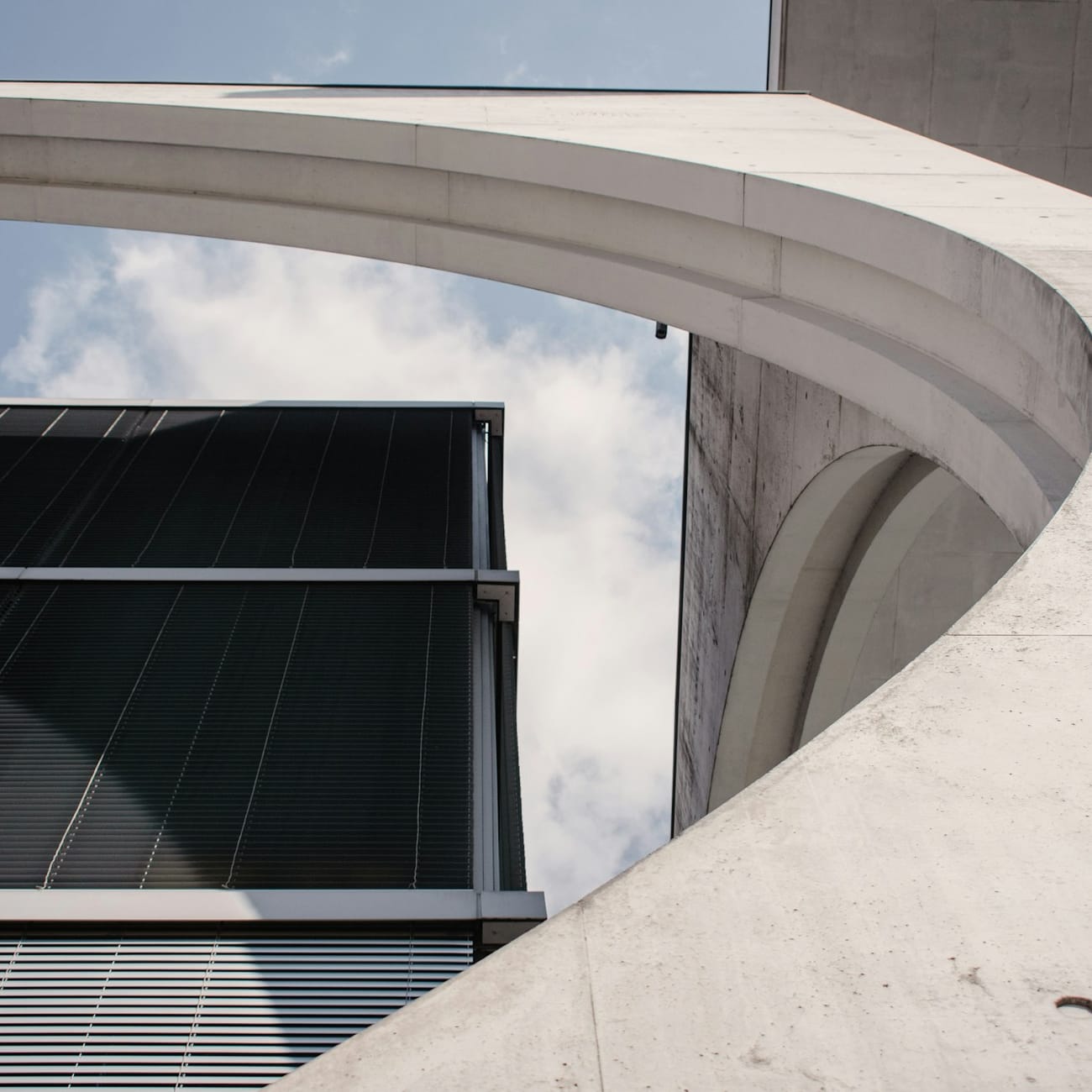 Curved concrete architecture against a glass facade and open sky